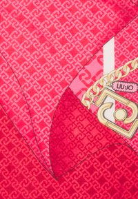 Tessuto rosa a fantasia con forme sovrapposte, arricchito da una catena dorata e un'etichetta con la scritta "LIU JO" su un lato.