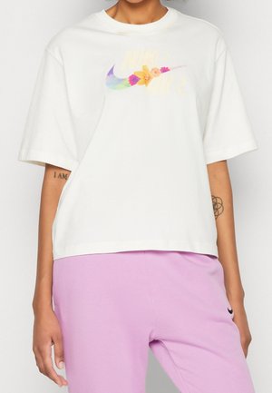 White cotton t-shirt with short sleeves featuring a multicolored "Nike Air" graphic and floral accents on the front, worn with lavender pants.