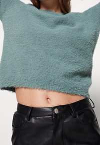 Suéter corto de teal claro hecho de material suave con un escote amplio, combinado con pantalones de cuero negro de cintura alta con cierre de botón.