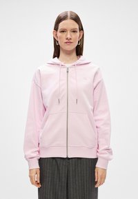 Ružová zipsová mikina s kapucňou, prednými vreckami a rebrovanými manžetami. Obsahuje jednoduché logo na hrudi a hladkú zmes bavlny.