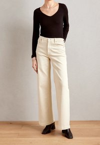 Jeans beige a gamba larga in denim di cotone con vita alta, dotati di tasche frontali e chiusura con bottone. Abbinati a un top nero a maniche lunghe.