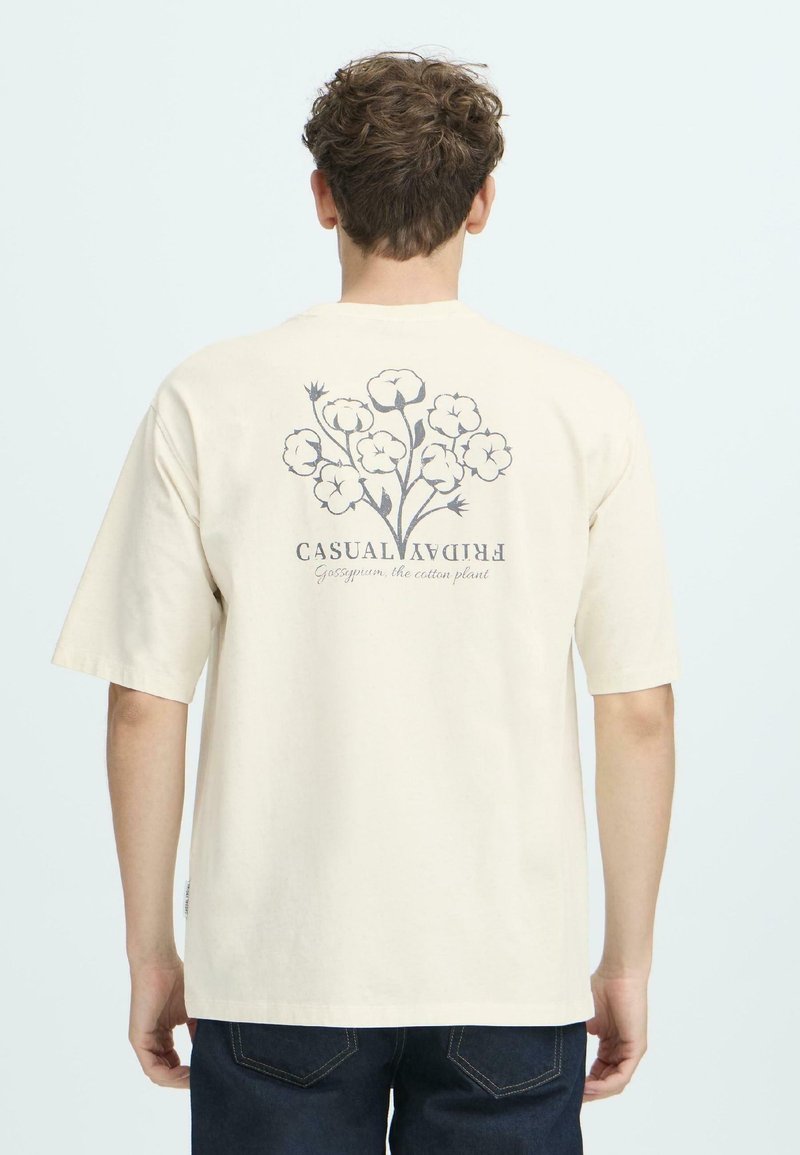 Kortærmet crème bomulds t-shirt med et grafisk motiv af en bomuldsplante på ryggen, med teksten "Casual Friday" under.