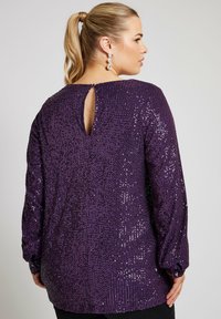 Lila paljetterad topp med långa ärmar, med en nyckelhålsöppning bak och knäppta manschetter. Slät textur med glittrande detaljer.