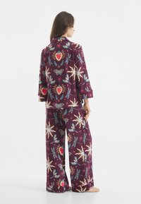 Paarse pyjama-set met een patroon van harten, zonnen en vlinders. Ruimvallend, met driekwart mouwen en brede broeken.