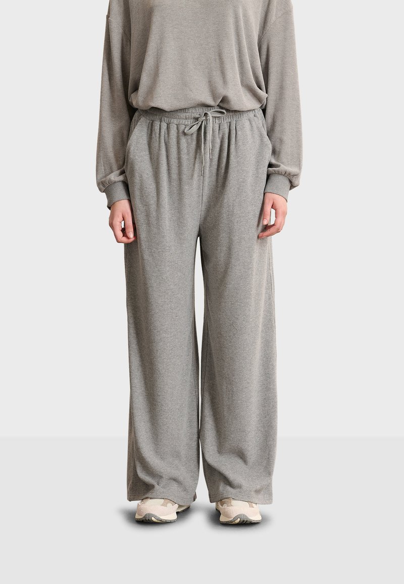 Grå högmidjade sweatpants med dragsko i midjan, vida ben och mjuk, slät textur, kombinerat med beiga sneakers.