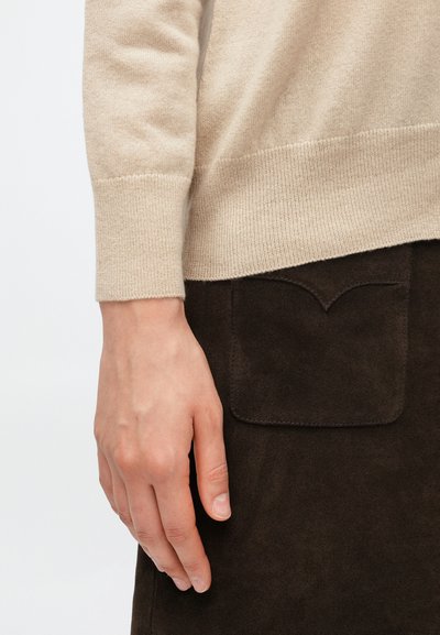 Bēšas vilnas sajaukuma džemperis ar ribotām aprocēm, kopā ar tumši brūnu zamšādas svārku ar izliekta augšdaļas detaļu un kabatu.