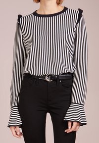Blusa a righe in bianco e nero, tessuto leggero, scollo rotondo, maniche svasate e dettagli arricciati sulle spalle. Indossata con jeans neri.