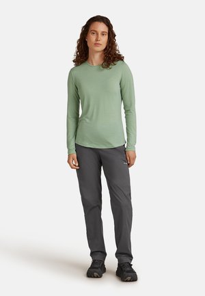Lichtgroen langemouwen shirt gecombineerd met donkergrijze broek. Het shirt heeft een ronde halslijn en een relaxte pasvorm, terwijl de broek zijvakjes heeft.