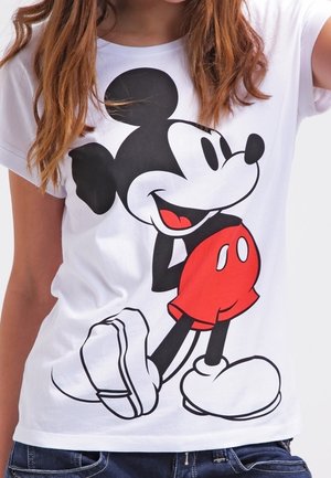 Jeune personne portant un T-shirt blanc avec un grand graphisme de Mickey Mouse en short rouge et chaussures blanches.