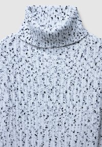 Pull à col roulé bleu clair avec un motif de tricot texturé, featuring des éclats noirs. Design côtelé autour du cou et du corps.