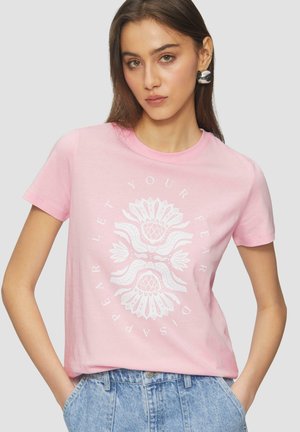 Pink cotton t-shirt featuring white floral graphic design. Short sleeves, round neckline, relaxed fit, worn with high-waisted denim shorts.