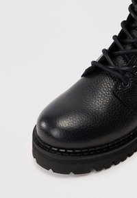 Musthave mustad nahkkingad tekstuuriga viimistlusega, ümar nina ja paks must kummitald. Geschmae lace-up sulgemine ja kontrastne õmblus.