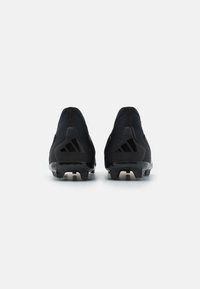 Par de botas de fútbol Adidas negras mostradas desde atrás, destacando las suelas texturizadas y los detalles del logo en los talones sobre un fondo blanco.