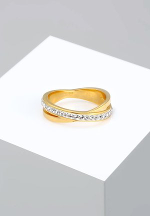 Anello in oro caratterizzato da un design intrecciato con una fascia abbellita da pietre trasparenti, superficie liscia e finitura lucida.