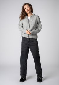 Gray knitted cardigan with a high collar, front buttons, and textured finish, paired with black wide-leg jeans and black shoes.