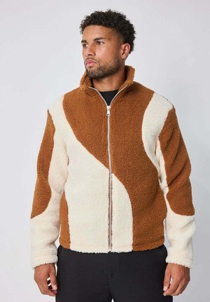 Veste en polaire marron et crème avec un col montant et une fermeture éclair complète, présentant un design en blocs de couleur courbé et une surface texturée.