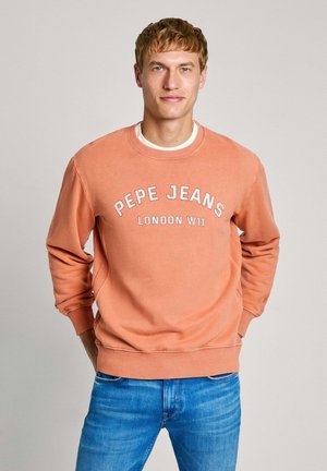 Sudadera de cuello redondo de Pepe Jeans en coral deslavado, con texto blanco "PEPE JEANS LONDON W11" y puños, cuello y dobladillo acanalados. Combinada con jeans azules.