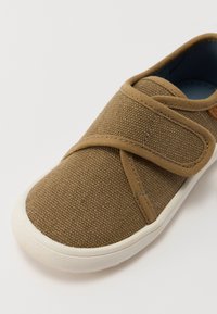 Braune Canvas-Schuhe mit strukturierter Oberfläche, verstellbarem Klettverschluss und weißer Gummisohle. Das Innere ist mit blauer Fütterung versehen.