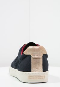 Sneaker blu navy con una tomaia in tessuto testurizzato, accentuato da un tallone metallico dorato e una suola in gomma bianca. Presenta un sottile rivestimento interno rosso.
