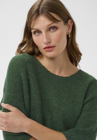Grüner Strickpullover mit weiter Passform, weitem Ausschnitt und strukturierter Stoff. Lange Ärmel, weiches Finish und leichte Farbvariationen.