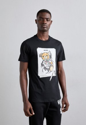 Sort bomulds T-shirt med et bjørn illustration iført butterfly og tekst, korte ærmer, rund hals, båret med sorte bukser.