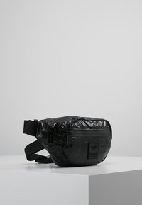 Czarna nylonowa saszetka na biodra z błyszczącą powierzchnią, zamykanymi komorami, regulowanym paskiem i wyraźnym logo na przodzie.
