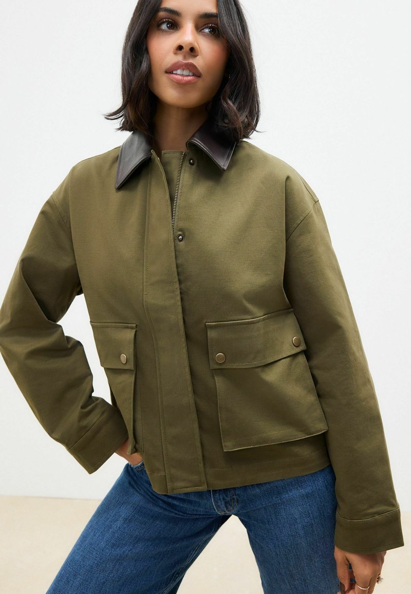 Grüne Leinjacke mit braunem Kragen, Druckknöpfen und zwei Vorderaschen. Verfügt über eine lässige Passform und sichtbare Nähte.
