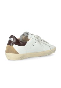 Sneaker bianche a taglio basso con suola beige, toppa sul tallone marrone, dettaglio in suede e lacci bianchi inclinati a destra su uno sfondo bianco.