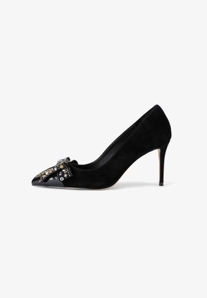 Décolleté nera in suede con tacco alto e punta affilata, caratterizzata da un inserto in pelle verniciata nera lucida e da decorazioni sul davanti.