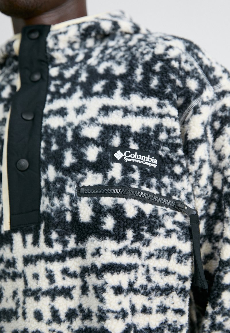 Polarowy pulower Columbia w kolorze czarnym i kremowym, z teksturowanym wzorem, kieszenią na zamek, napami oraz naszywką z logo na torsie.