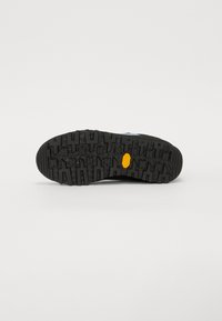 Schwarze Gummi-Außensohle mit tiefen Rillen und einem gelben Logo, das ein strukturiertes Muster für Grip und Stabilität aufweist.