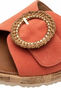 Sandalo slide in suede corallo con un accentuato cerchio intrecciato in vimini e tonalità oro. Presenta una suola simile al sughero e una parte superiore morbida e testurizzata.