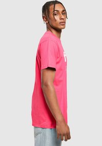 Camiseta de algodón rosa con mangas cortas y cuello redondo, que muestra texto gráfico blanco en el frente, con un ajuste regular y una textura suave.