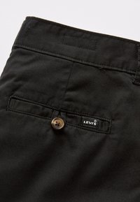 Pantalon en tissu noir à la texture lisse, avec un bouton marron et une petite étiquette noire Levi's sur la poche arrière.