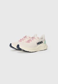 Running shoes with a light pink mesh upper, navy sole, and green accents. Features prominent HOKA branding on the side.