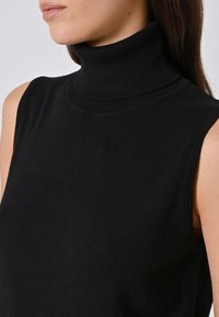 Zwarte mouwloze coltrui van zacht, ribbelstof. Voorzien van een hoge nek met een snug fit en een gladde textuur, minimalistisch ontwerp.