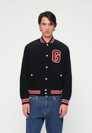 Veste de varsity en velours côtelé noir avec un col côtelé rayé rouge et blanc, des boutons pression blancs et un patch "G" rouge sur la poitrine.