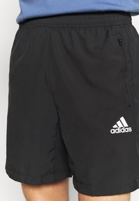 Bermudas deportivas negras hechas de un material ligero, con una cintura elástica y un bolsillo con cremallera, y el logo de Adidas en blanco.