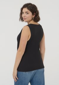 Top nero senza maniche dal design aderente con scollatura rotonda. Tessuto morbido con un orlo posteriore leggermente allungato, abbinato a jeans blu a vita alta.