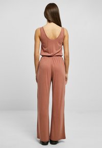 Rosa jumpsuit med scoop rygg, elastisk midje, og vide ben, laget av myk stoff. Glatt tekstur og minimalistisk design.