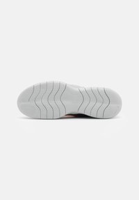 Semelle de chaussure présentant une surface en caoutchouc blanc texturé avec des rainures courbées et des points pour l'adhérence, accentuée par un petit logo de marque.