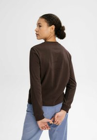 Brauner Langarmshirt mit Rundhalsausschnitt, glatter Textur und enganliegenden Bündchen, kombiniert mit hellblauen Cordhosen.