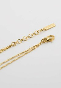 Collana in metallo dorato con link circolari, dotata di un gancio e un'etichetta contrassegnata "JETTE". La texture è liscia con una finitura lucida.
