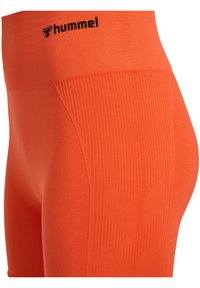 Oranje high-waisted leggings met een gladde textuur en verticale ribbelaccenten, en een zwart "hummel" logo op de tailleband.