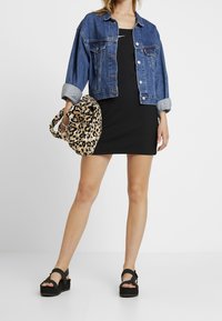 Jeansjacka med uppvikta ärmar, svart ribbat klänningsplagg och handväska med leopardskriv. Skorna är robusta svarta sandaler med remmar.