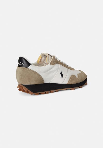 Μπεζ και λευκό αθλητικό παπούτσι με επάνω μέρος από σουέντ και δίχτυ, μαύρο τακούνι, λευκά κορδόνια και υφασμένο ελαστικό πέλμα. Διαθέτει ένα μικρό λογότυπο αλόγου.