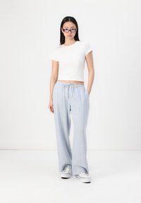Pantalons larges rayés bleu clair avec taille à cordon ajustable, associés à un t-shirt blanc à manches courtes ajusté et des baskets blanches.