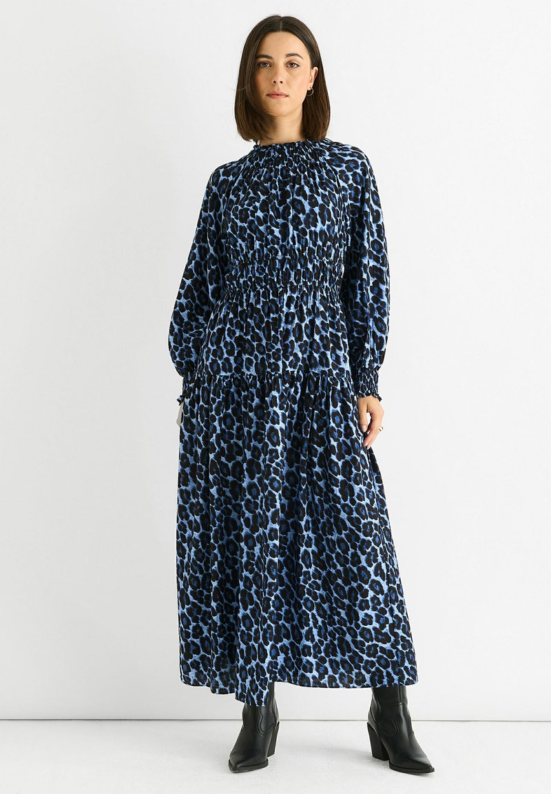 Long-sleeve, blue leopard print dress with a smocked waist, tiered skirt, and rounded neckline. Worn with black ankle boots.