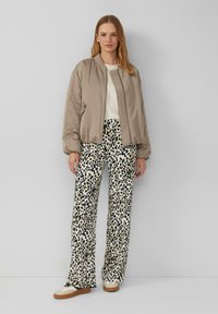 Helle beige Bomberjacke, weißes Oberteil, weit geschnittene Hose im Leopardenmuster, cremefarbene und braune Schuhe, glatte Textur, lässige Passform und auffälliges Muster.