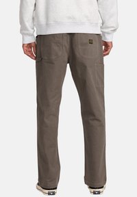 Bruine katoenen cargo pants met een rechte pijp, voorzien van twee achterzakken en een zijzak, gecombineerd met een grijze sweatshirt en sneakers.